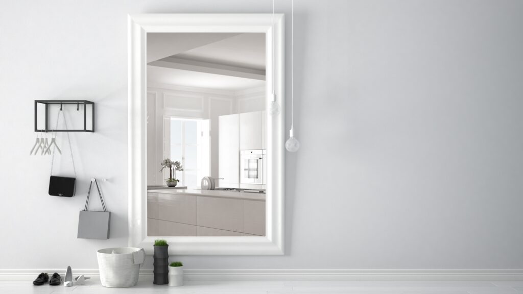 Modern gestalteter Eingangsbereich mit einem großen Spiegel, der eine Küche reflektiert und den Raum optisch vergrößert, neben minimalistischen Dekorationen und einer klaren, weißen Wand