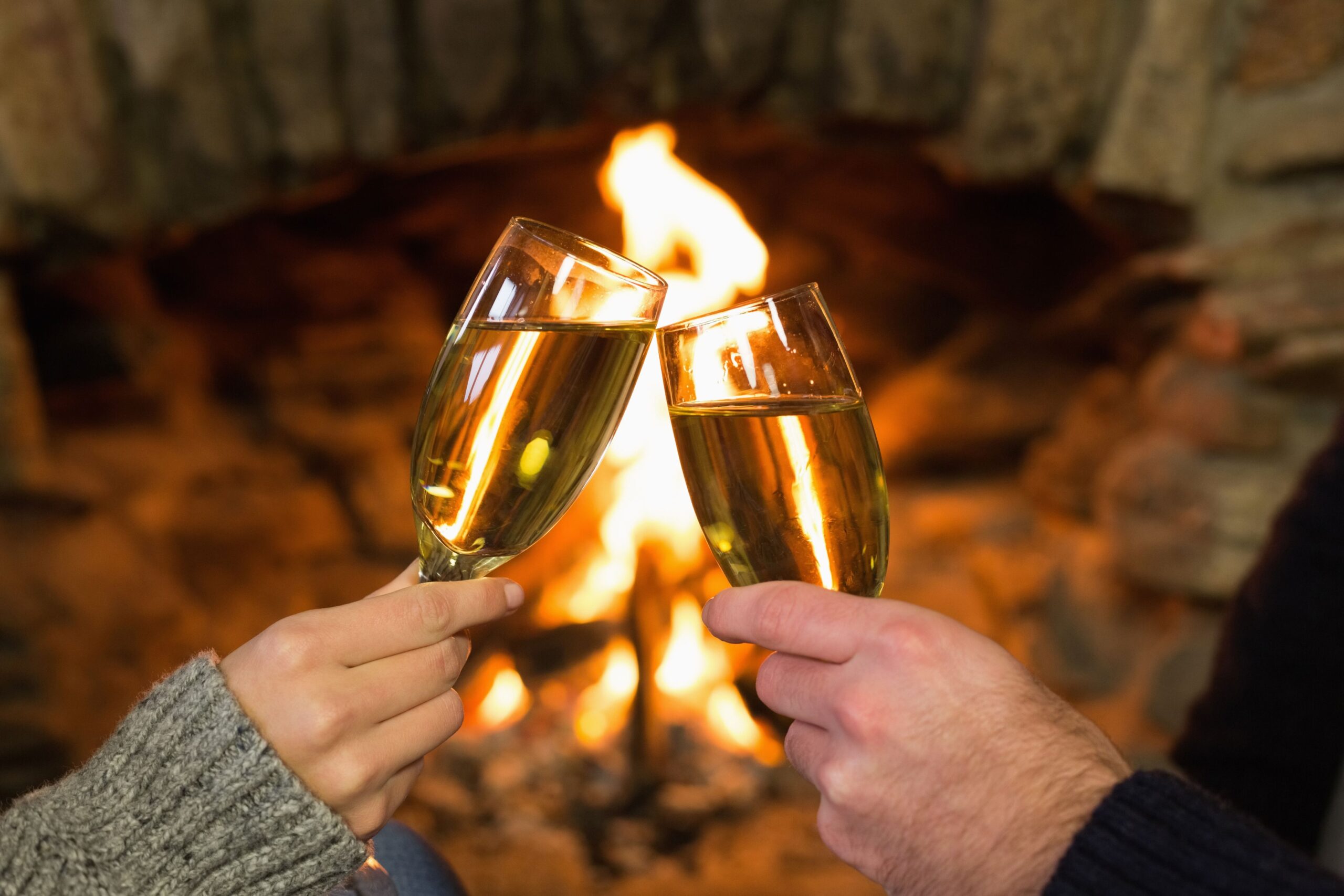 Zwei Personen stoßen mit Champagnergläsern vor einem knisternden Kamin an