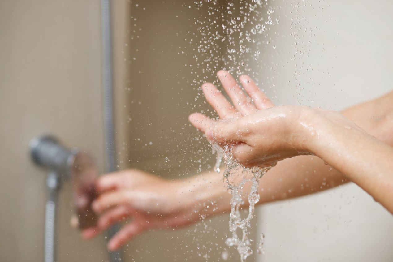 Nahaufnahme von Haenden unter Wasserstrahl in Dusche mit pflegeleichter Duschrueckwand Aluverbund
