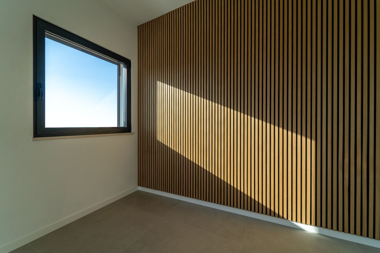 Akustikpaneele aus Holz in modernem Raum mit Fenster und Lichteinfall – wärmedämmende Wandverkleidung in Lamellenoptik