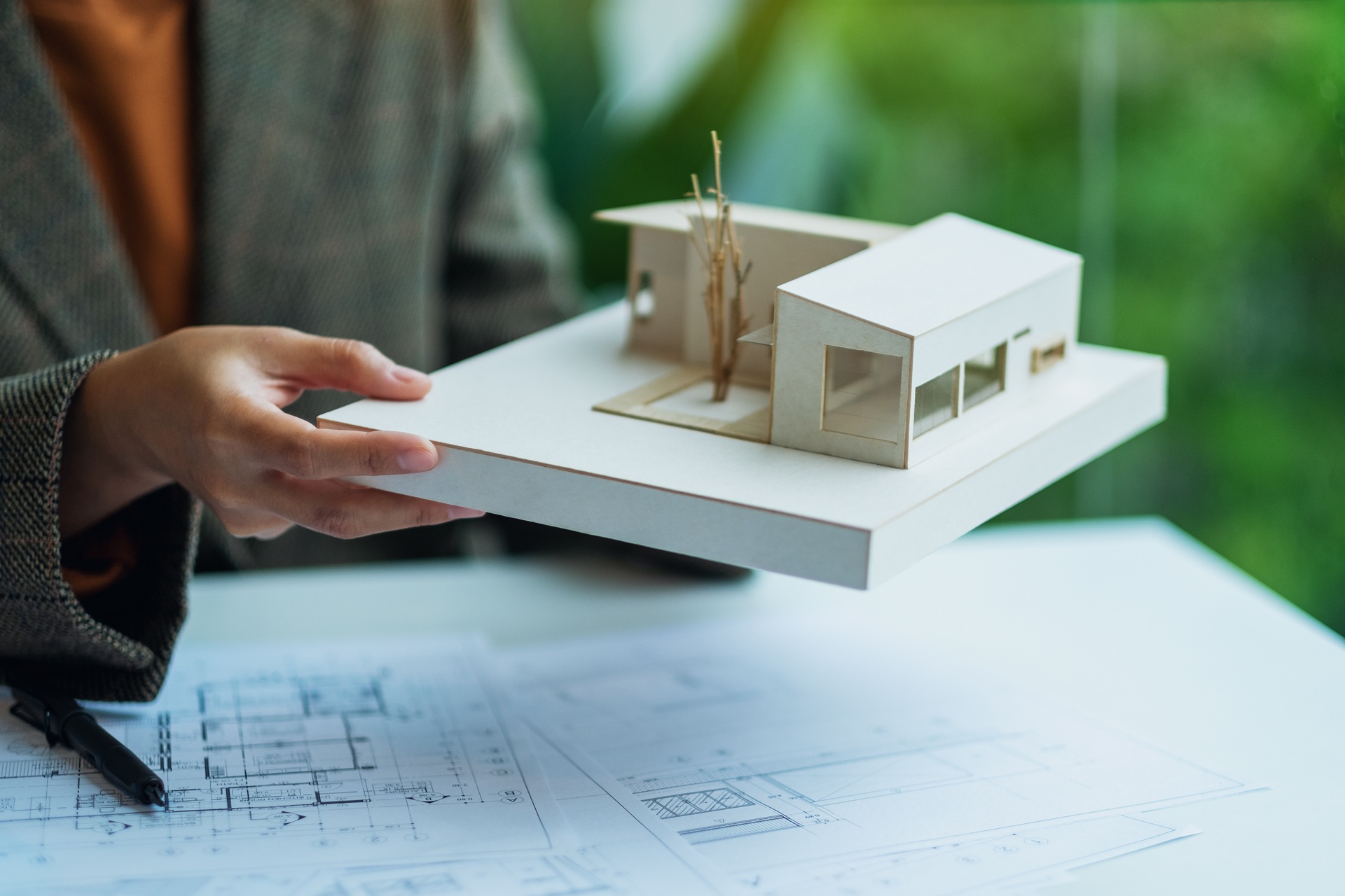 Person hält Architekturmodell über Bauplänen | Immobilienfinanzierung Düren